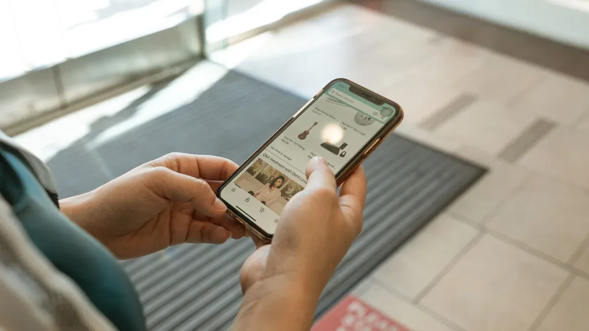 Close-up of hands holding a smartphone displaying an online shopping app in an indoor setting.