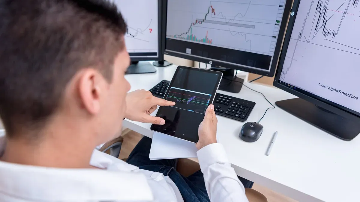 A stock trader analyzing cryptocurrency charts on multiple monitors and a tablet.
