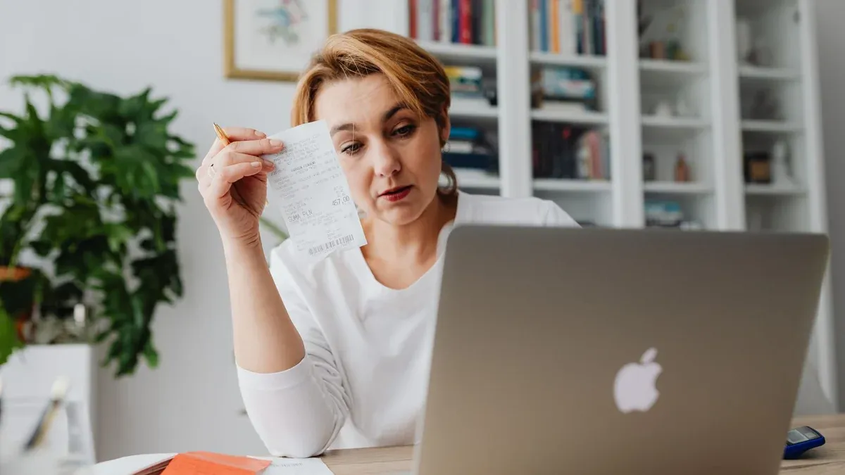 Woman concentrating on receipts while using a laptop, reflecting financial stress.