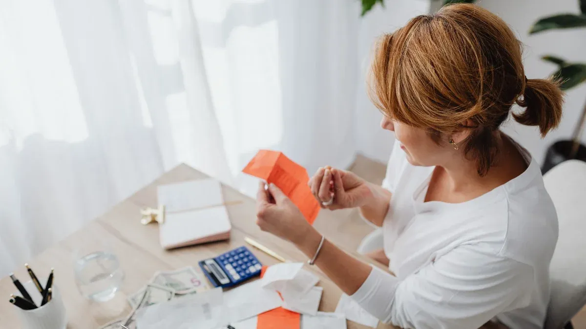A woman organizing her finances with bills and receipts at a home office desk using a calculator and laptop.