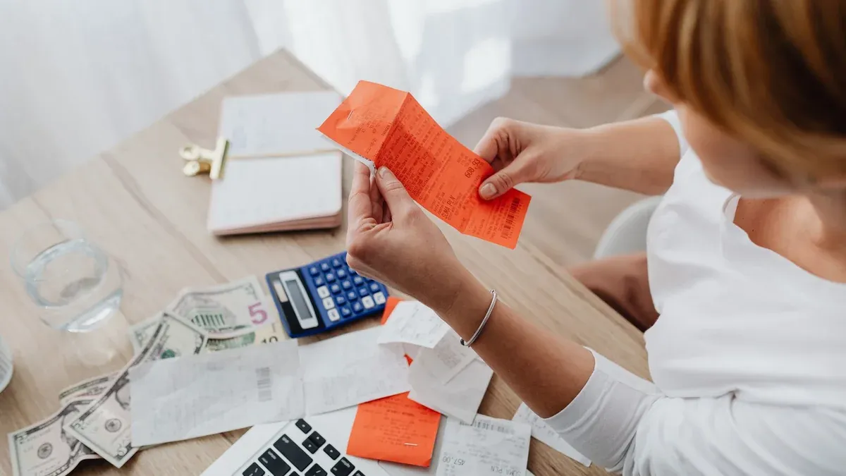 Woman using calculator and receipts at home office desk for finance management.