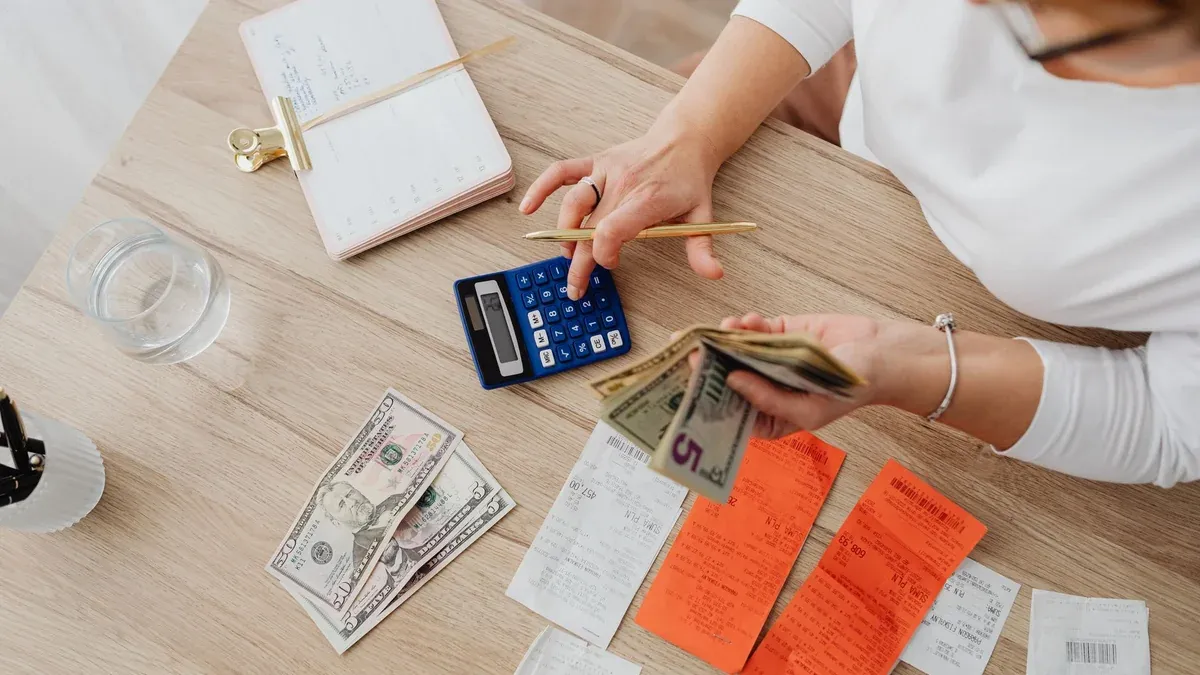 Overhead view of a person using a calculator to manage cash and receipts at a desk.
