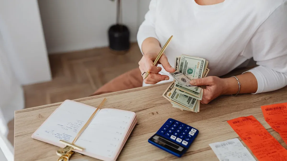 Woman sorting finances with a calculator, cash, and receipts at a desk.