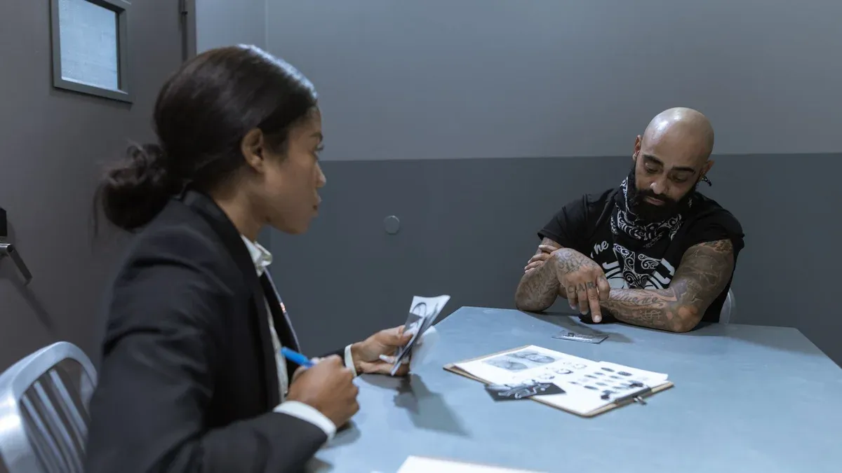 Police officer interrogating a suspect in an investigation room with documents and evidence on the table.