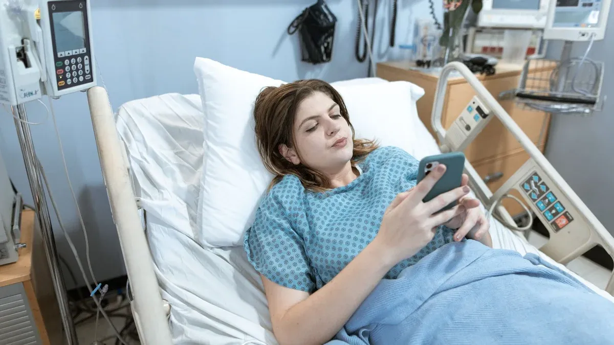 A young woman in a hospital bed using her smartphone while recovering.