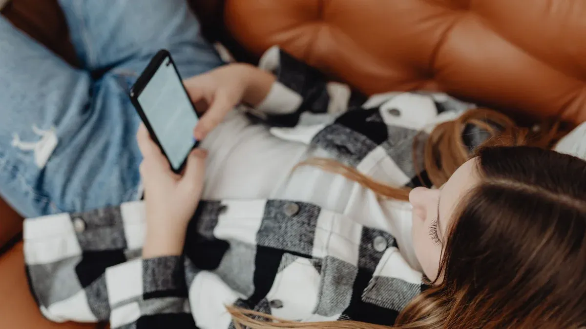 A teenager lying on a sofa, using a smartphone for social media browsing.