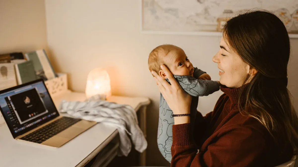 Mother holding baby while video calling from home office. Cozy and heartwarming indoor scene.