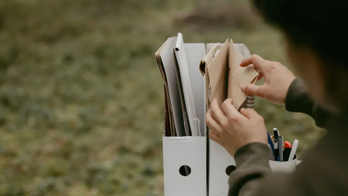 Person sorting documents in folders outdoors, hands visible, neutral tone.