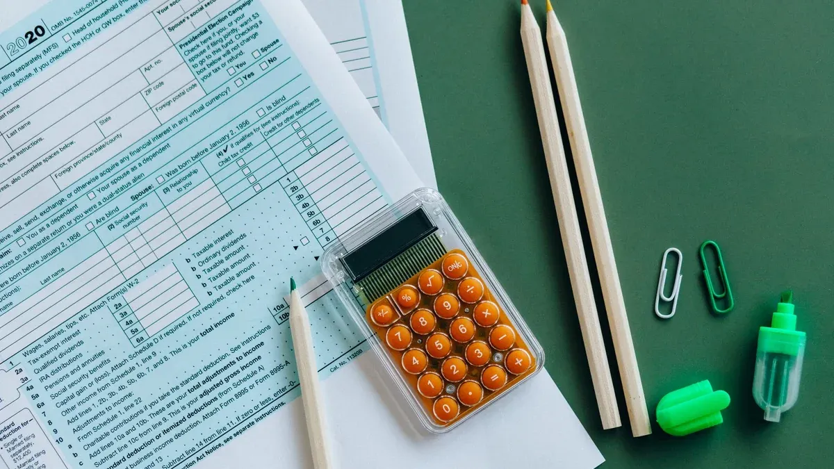 Flat lay of tax forms, calculator, pencils, and clips on green surface, ideal for finance or accounting themes.
