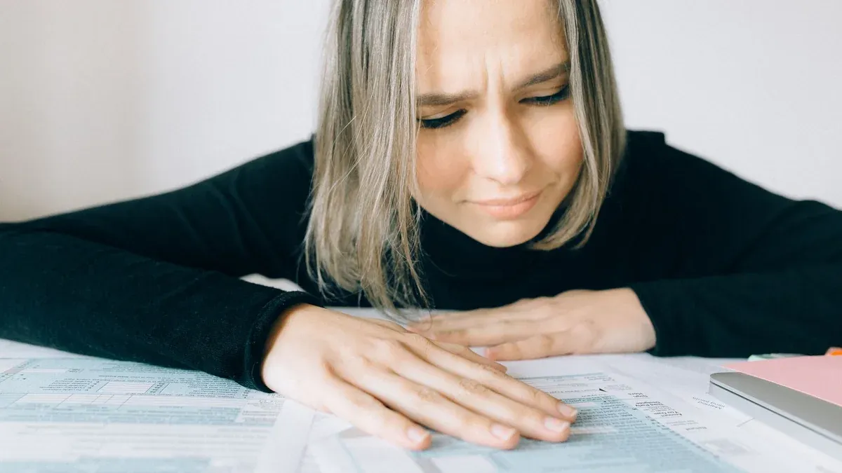A worried woman analyzing financial paperwork at her desk, signifying stress during tax season.