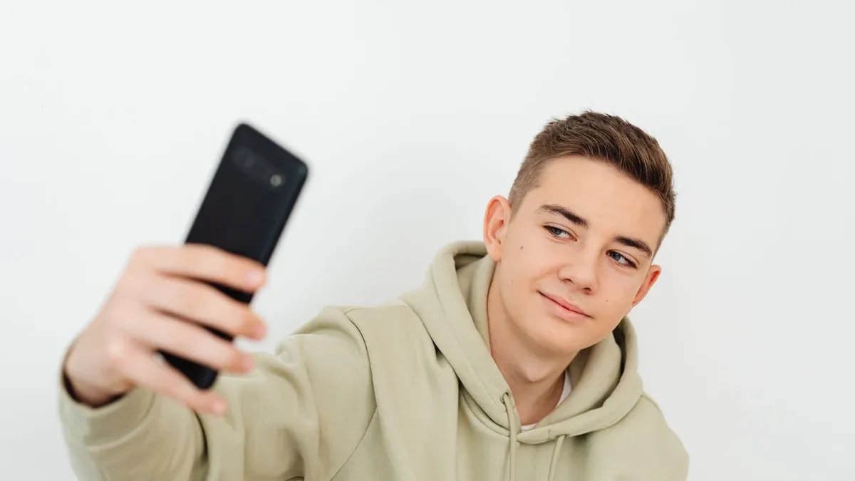 Teenager in hoodie taking a selfie indoors with a smartphone.