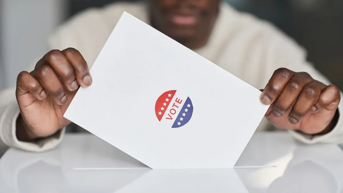 A voter placing a ballot into a box during an election. Focus on the act of voting.