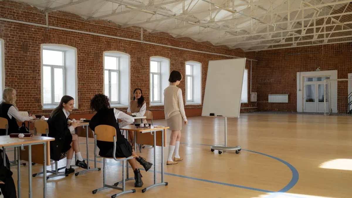Students in school uniforms engaged in a lesson with a teacher in a spacious classroom.