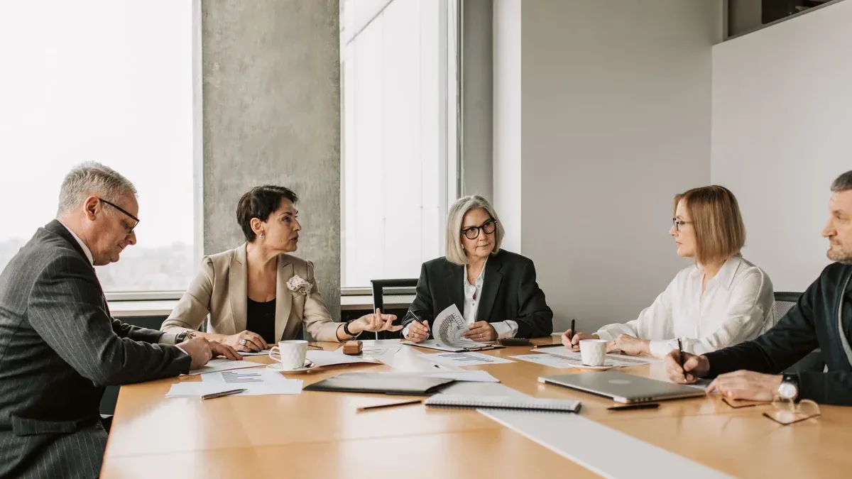 Five business professionals engaged in a meeting in a modern office setting, discussing documents and ideas.