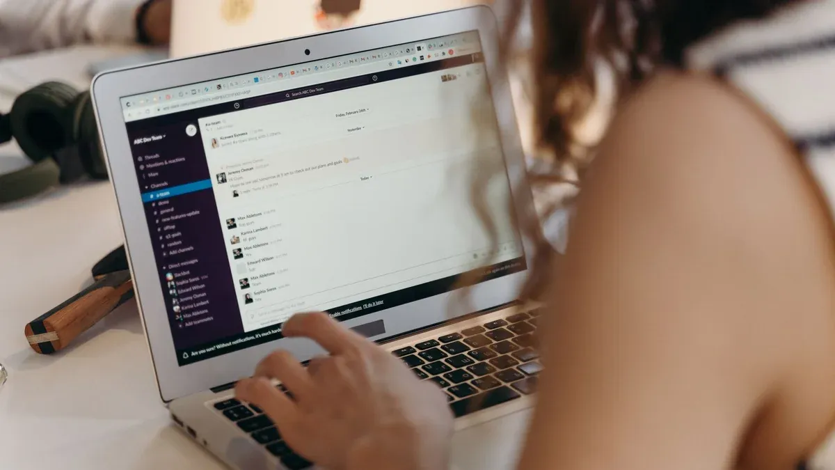 A businesswoman typing on a laptop in an office setting, using Slack for communication.