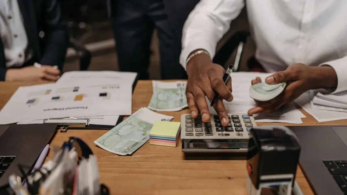 Professional setting with people handling cash and calculations using a calculator at a desk.