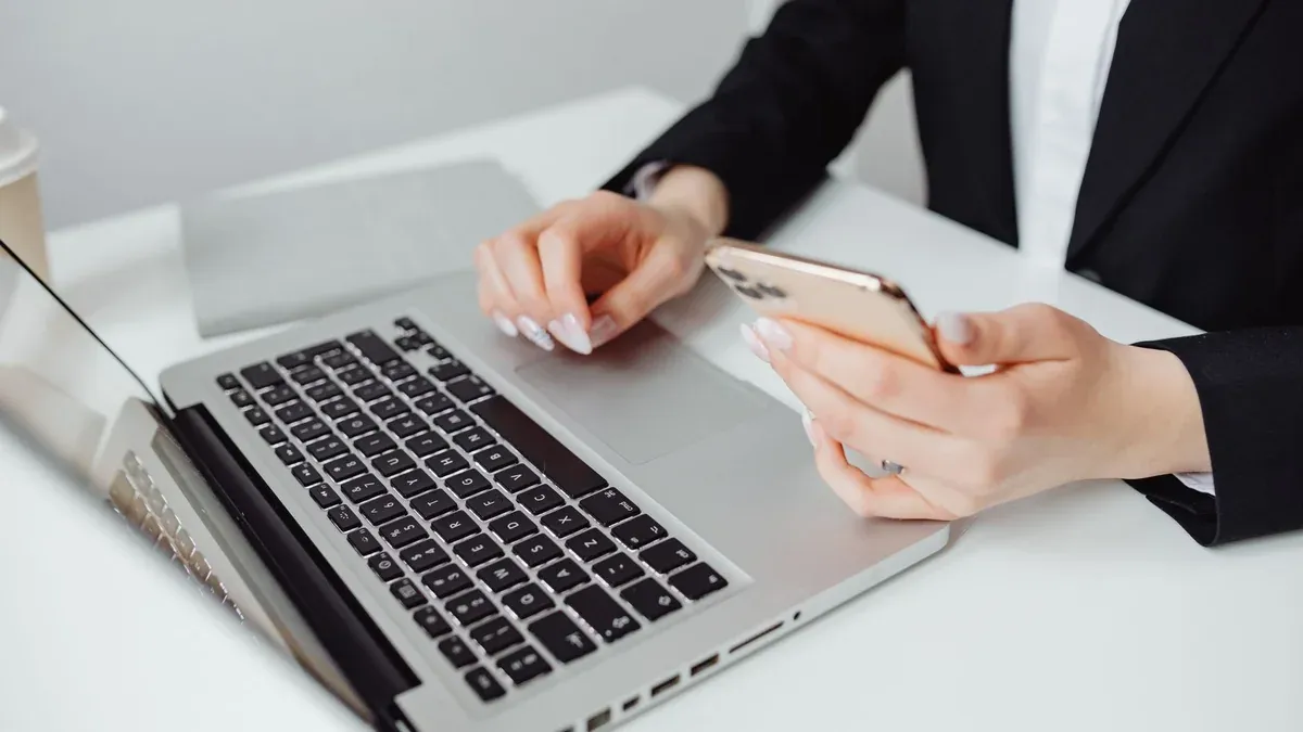 Professional woman in business attire using a laptop and smartphone at a desk.