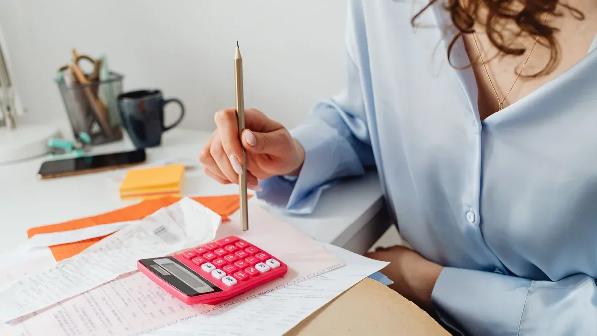 A woman is calculating expenses using a calculator and papers at her desk.