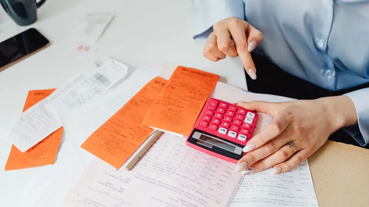 Businesswoman calculates expenses using receipts and calculator at desk. Ideal for finance, accounting themes.