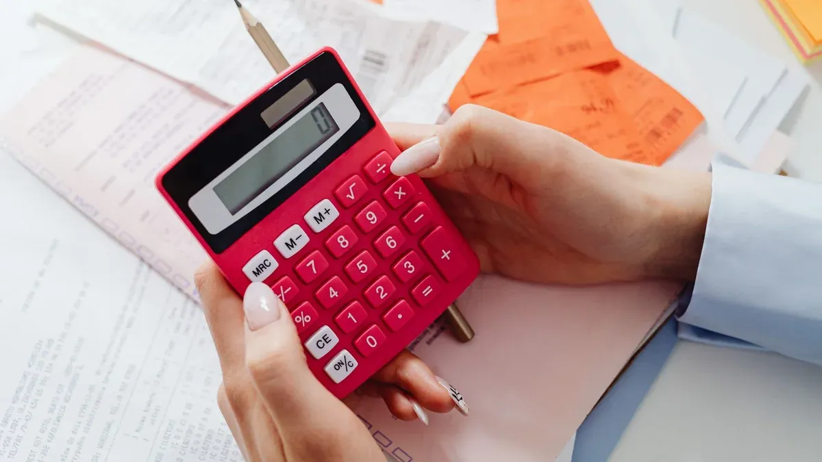 Close-up of hands holding a red calculator, managing finances with documents and receipts.