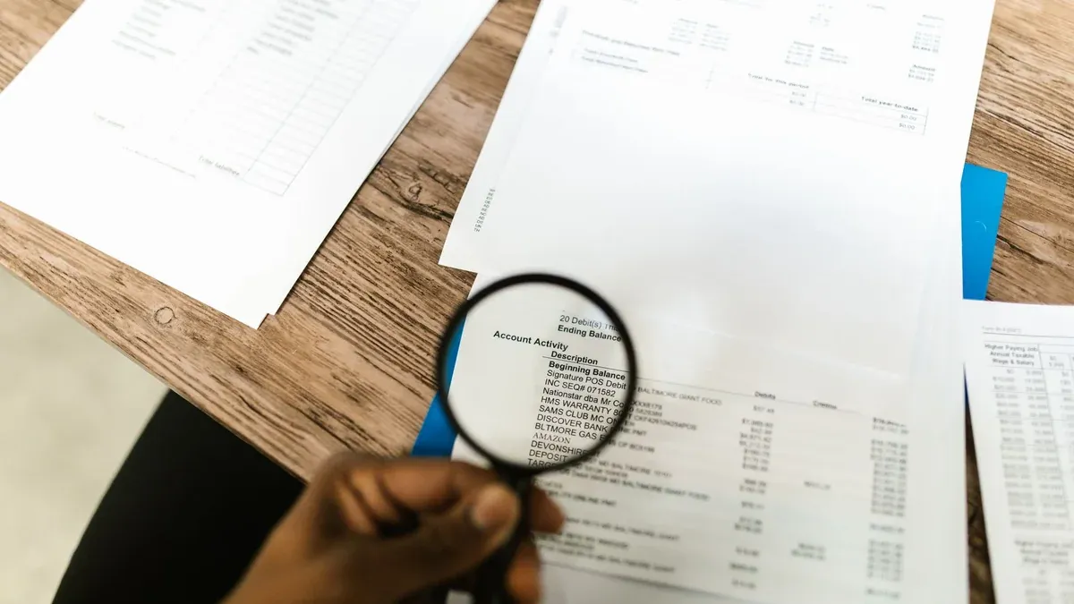 Close-up of hand using magnifying glass to review documents. Ideal for financial themes.