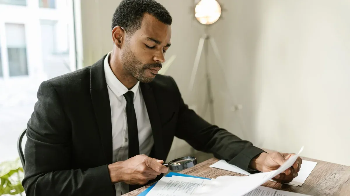 Professional man examines paperwork with magnifying glass at office desk, highlighting attention to detail.