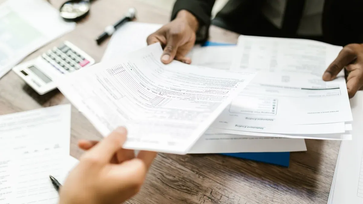 Two professionals exchanging documents in an office setting, focusing on paperwork and data analysis.