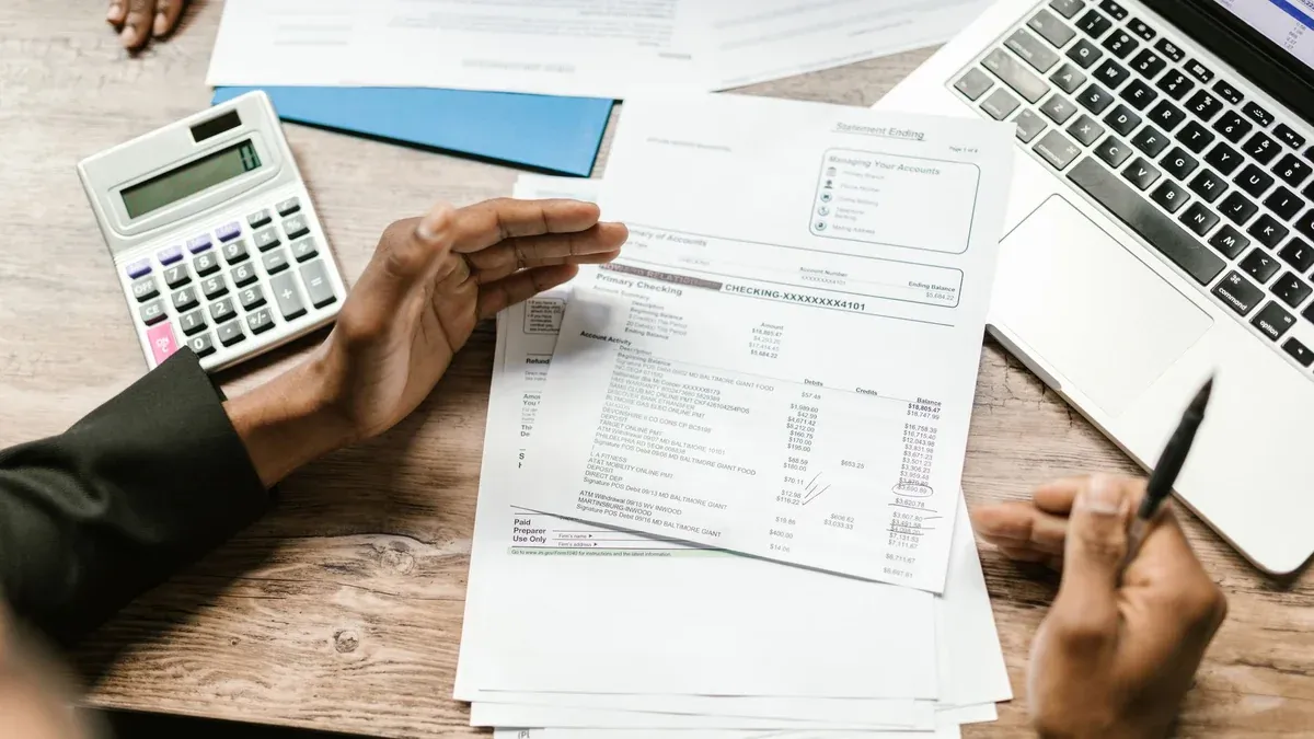 Hands holding financial documents with calculator and laptop on office desk, business analysis scene.
