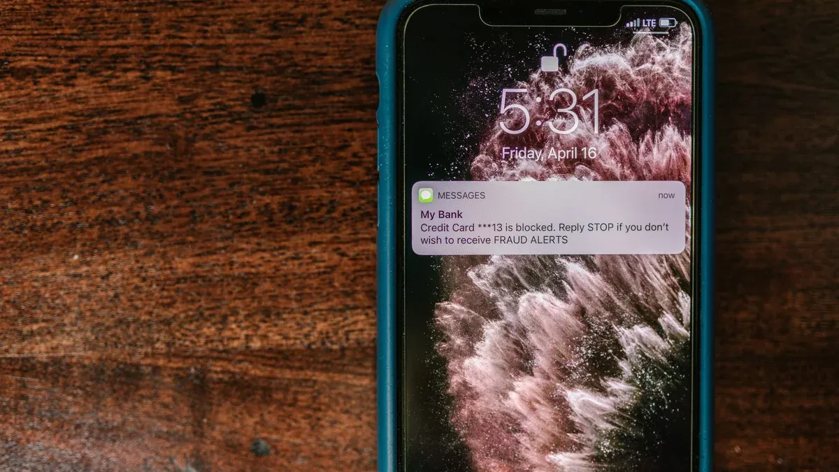 Close-up of smartphone displaying a fraud alert message on wooden surface.