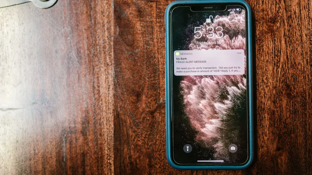 Close-up of a smartphone displaying a fraud alert message on a wooden table.