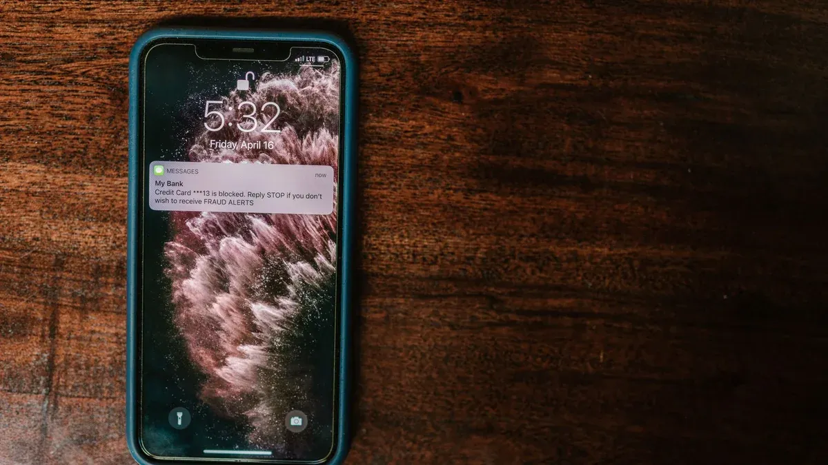 Close-up of smartphone on wooden surface displaying a bank alert message.