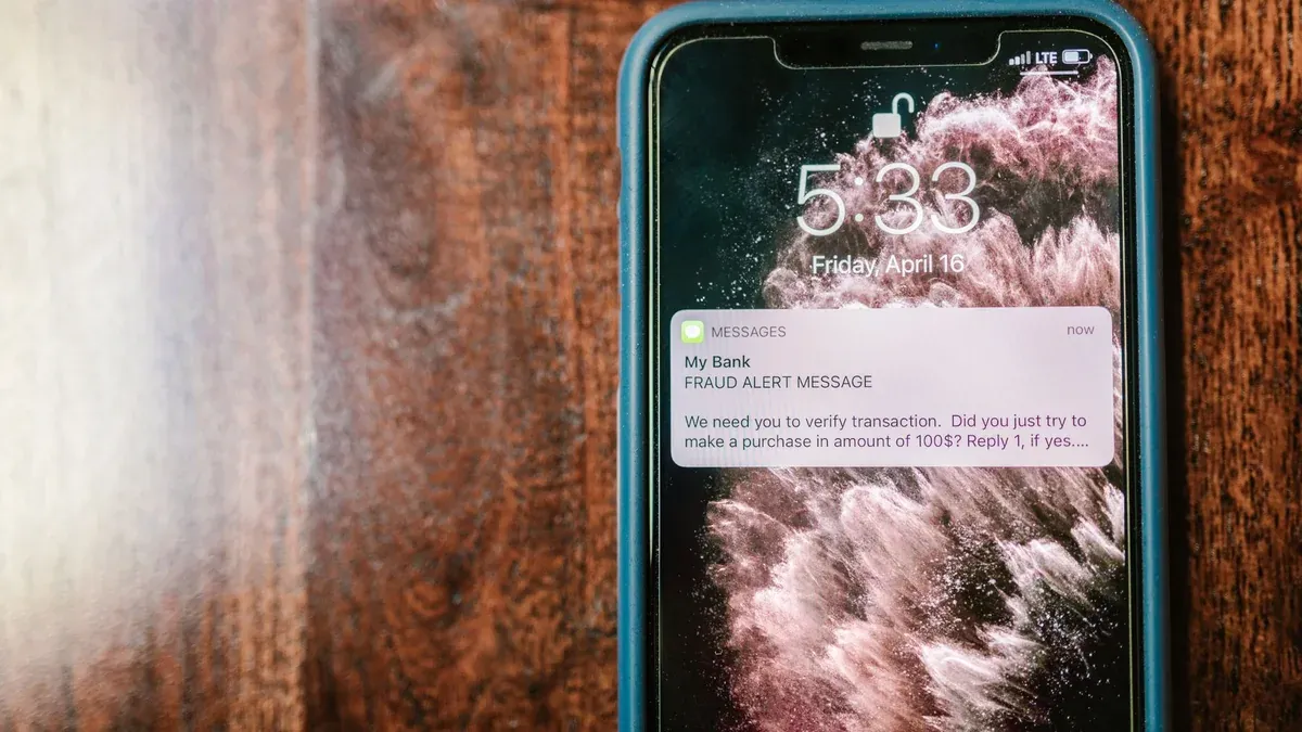 Close-up of a smartphone displaying a fraud alert notification on a wooden surface.