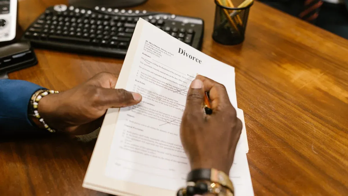A person signs official divorce documents at an office desk.