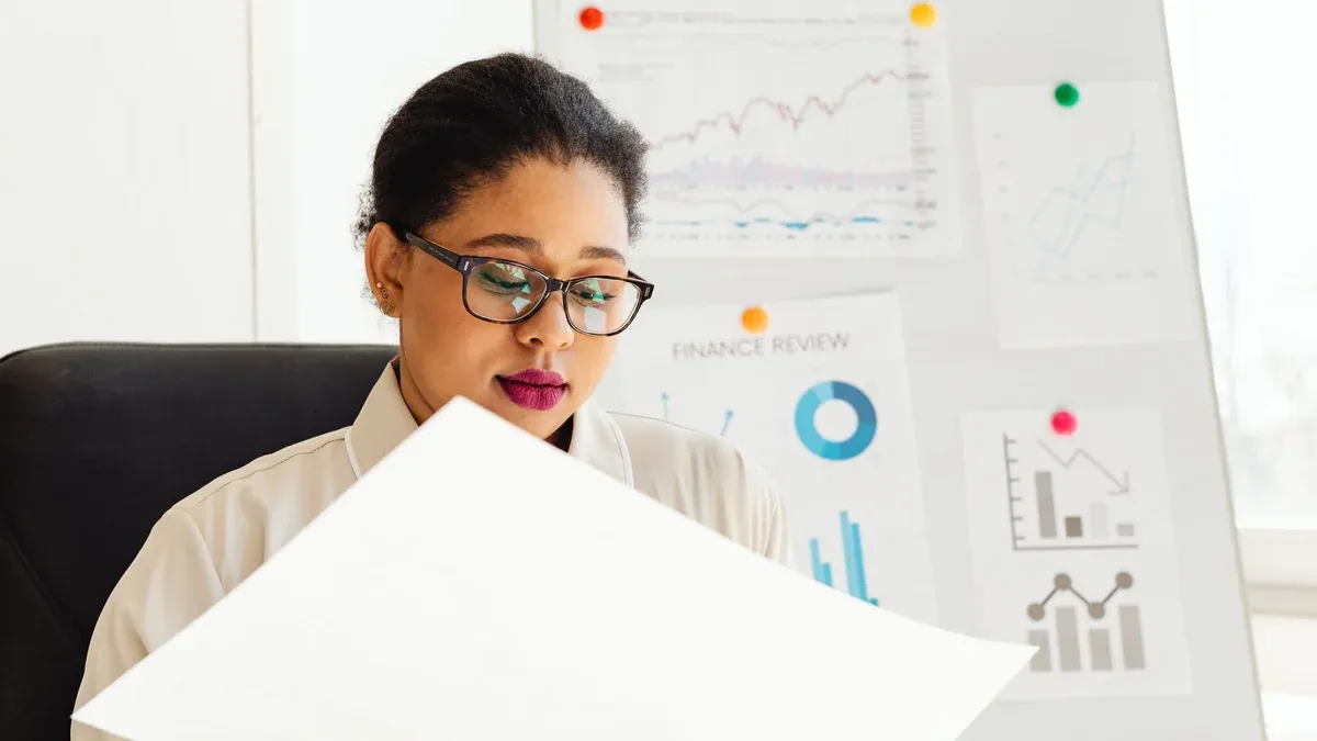 An African American woman studying financial charts and graphs in an office.