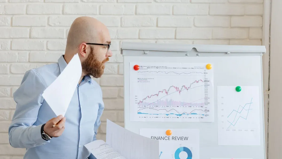 Bald businessman in smart casual attire analyzing financial charts on a whiteboard in an office setting.