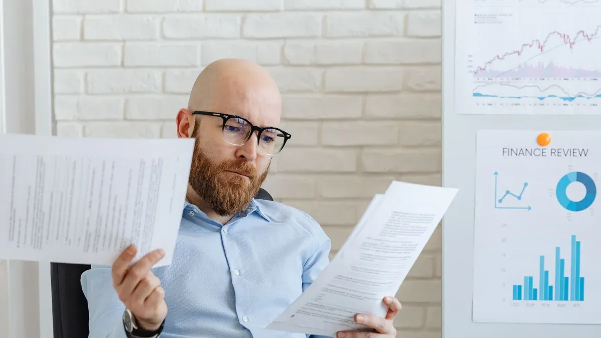 Bald bearded businessman reading financial documents in modern office setting.