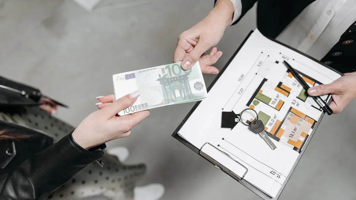 Close-up of a real estate transaction with euro bill, keys, and floor plan.