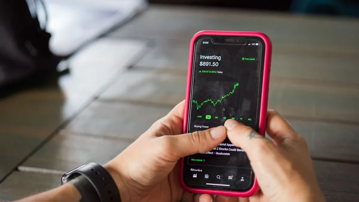 A person holding a smartphone with a stock market app displaying analytics and stock prices.