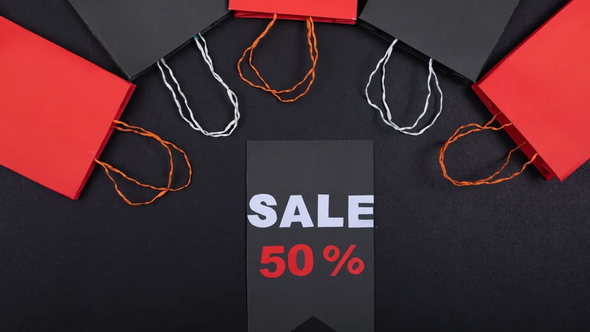 Flat lay of black and red shopping bags surrounding a sale sign with 50% discount on black background.