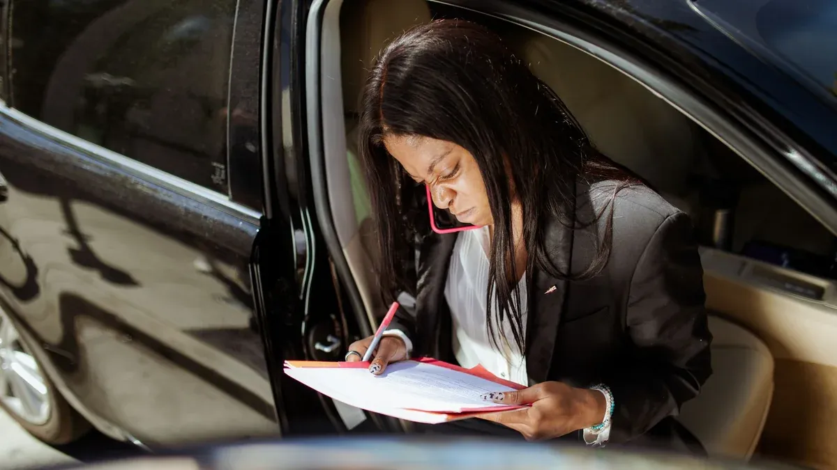 A focused businesswoman analyzes documents while sitting in her car.