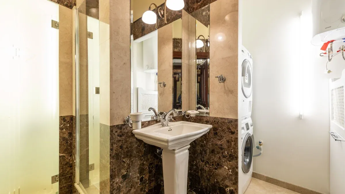 Elegant bathroom interior featuring marble walls, a pedestal sink, and a washer-dryer unit.