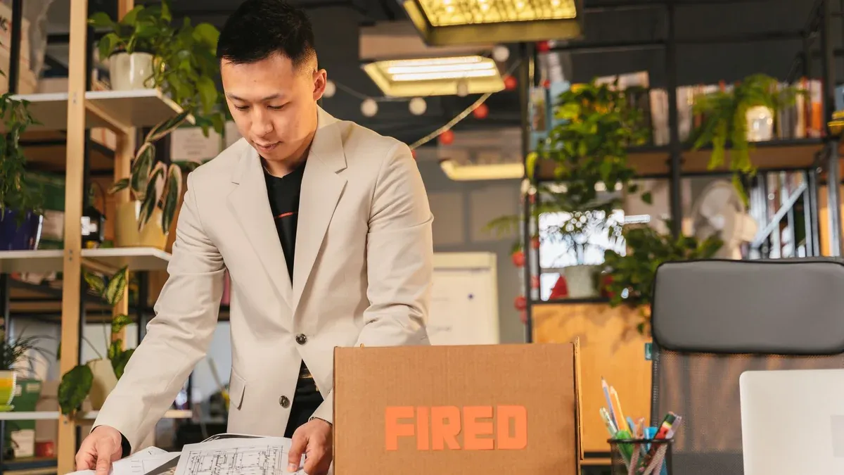 An employee packing documents into a box labeled 'FIRED' in an office environment.