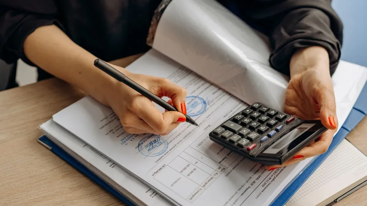 An accountant using a calculator and signing paperwork, showcasing financial analysis.