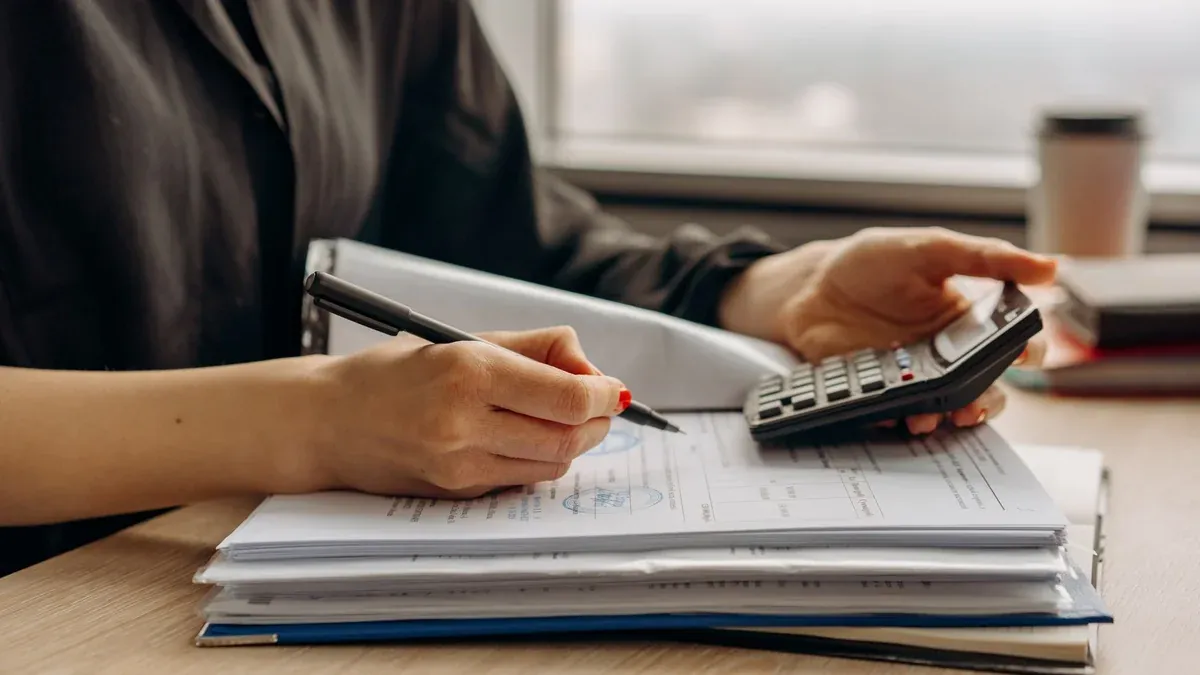 Close-up of person using a calculator with financial documents in an office.