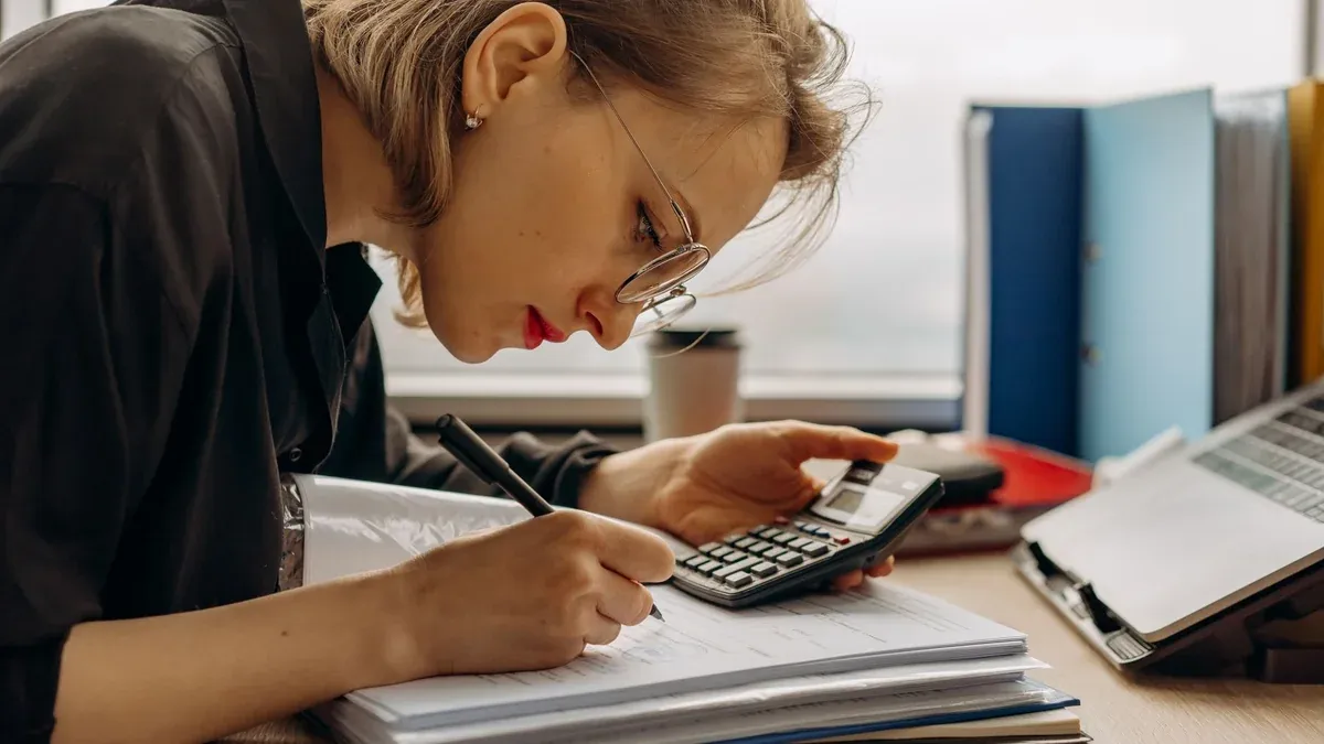 Young woman diligently working on accounting with a calculator and documents. Perfect for business and finance themes.