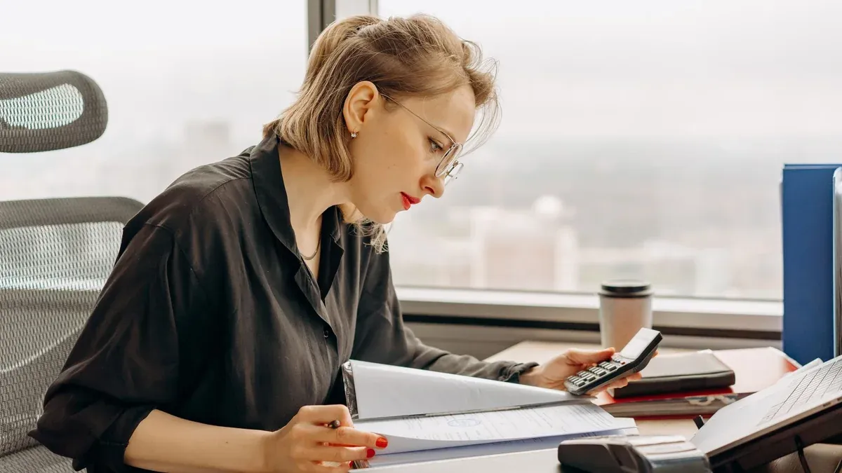 Woman accountant calculating financial documents at office desk.