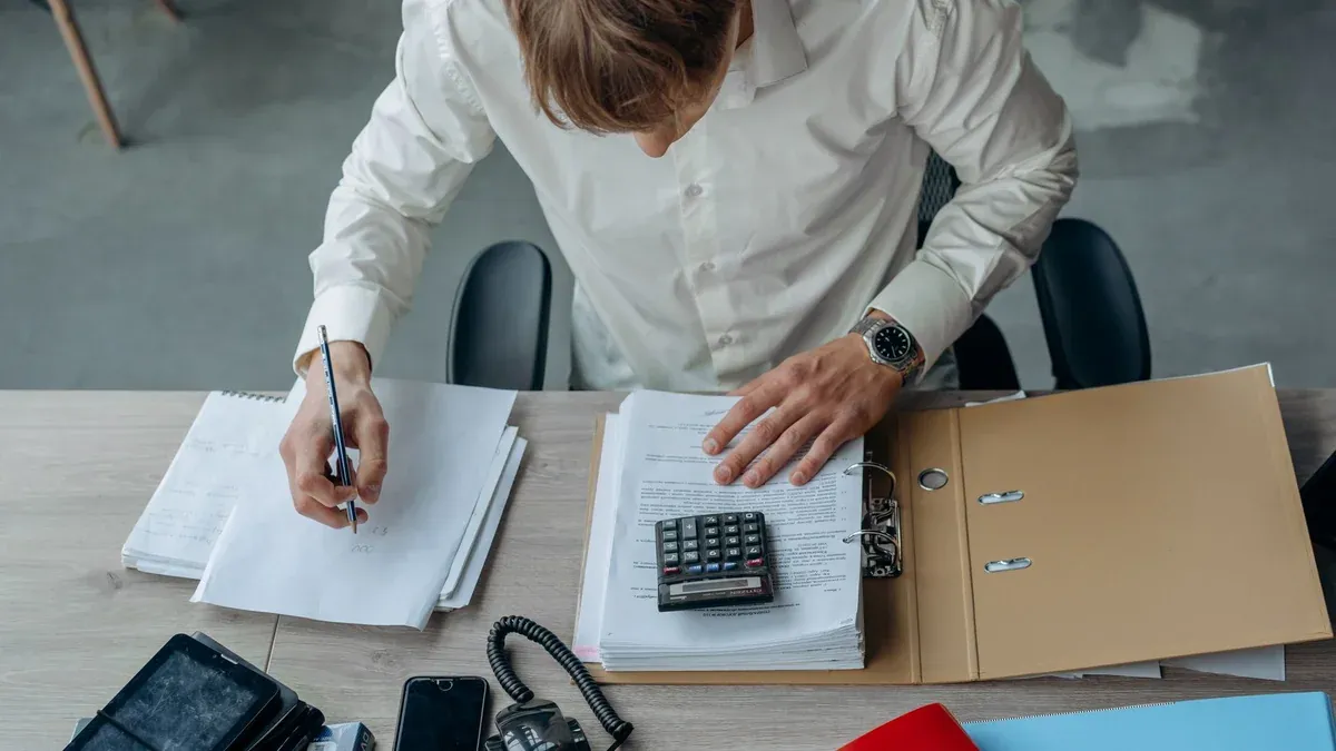 Man in an office reviewing financial papers with a calculator on a desk.