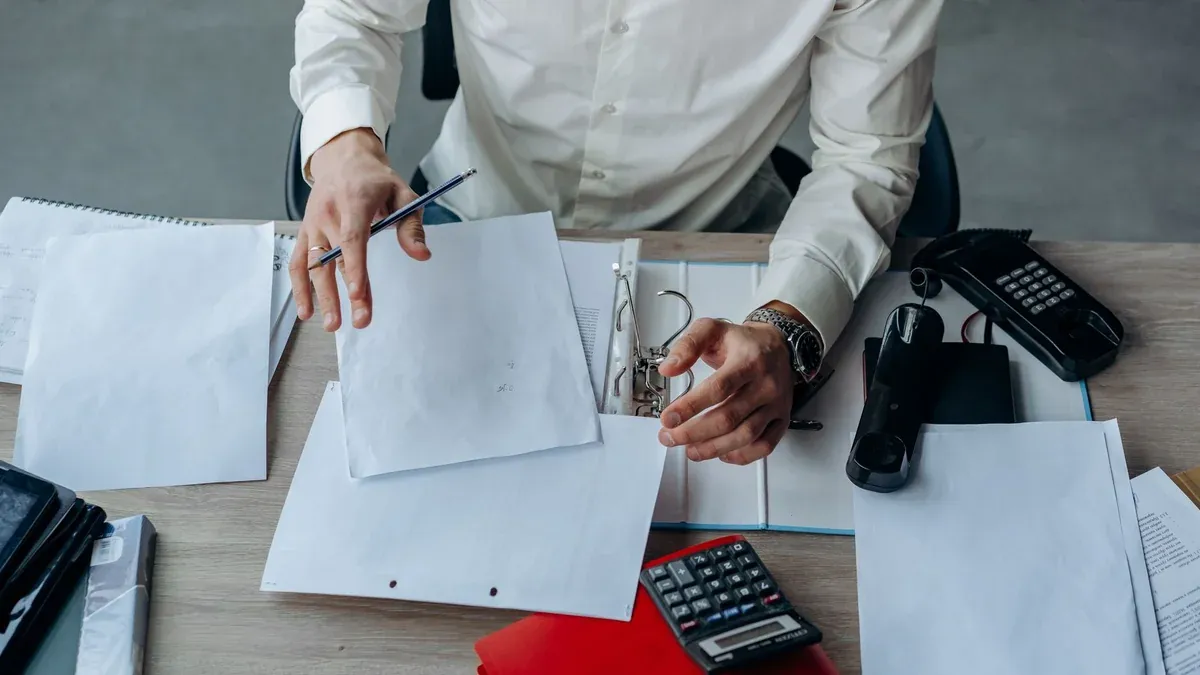 A business professional organizing documents at a busy office desk, emphasizing productivity.
