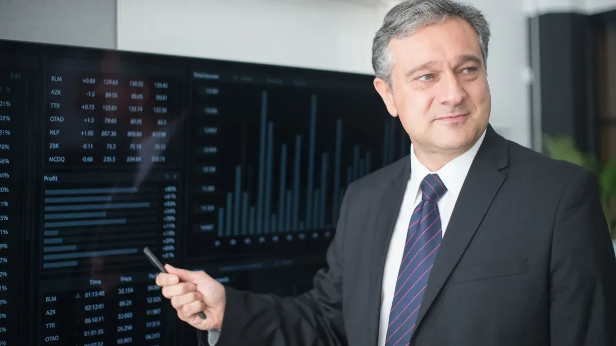 Professional man in suit reviewing financial charts on monitor, showcasing stock market trends.
