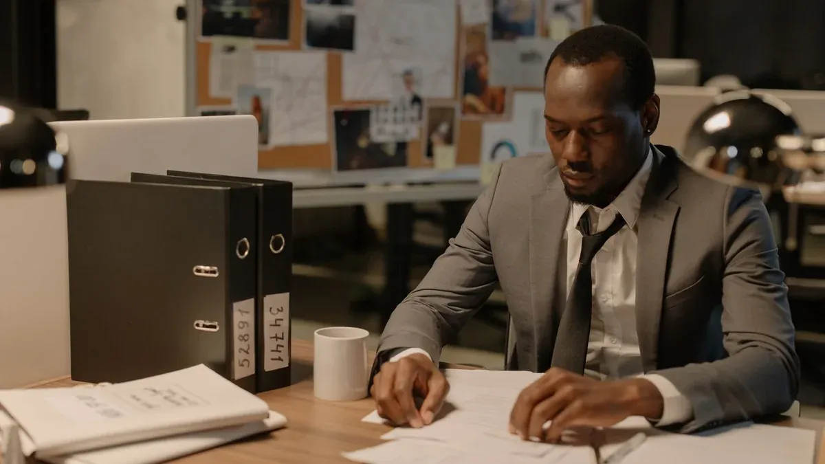 Man in business suit working late at office desk with documents and files.